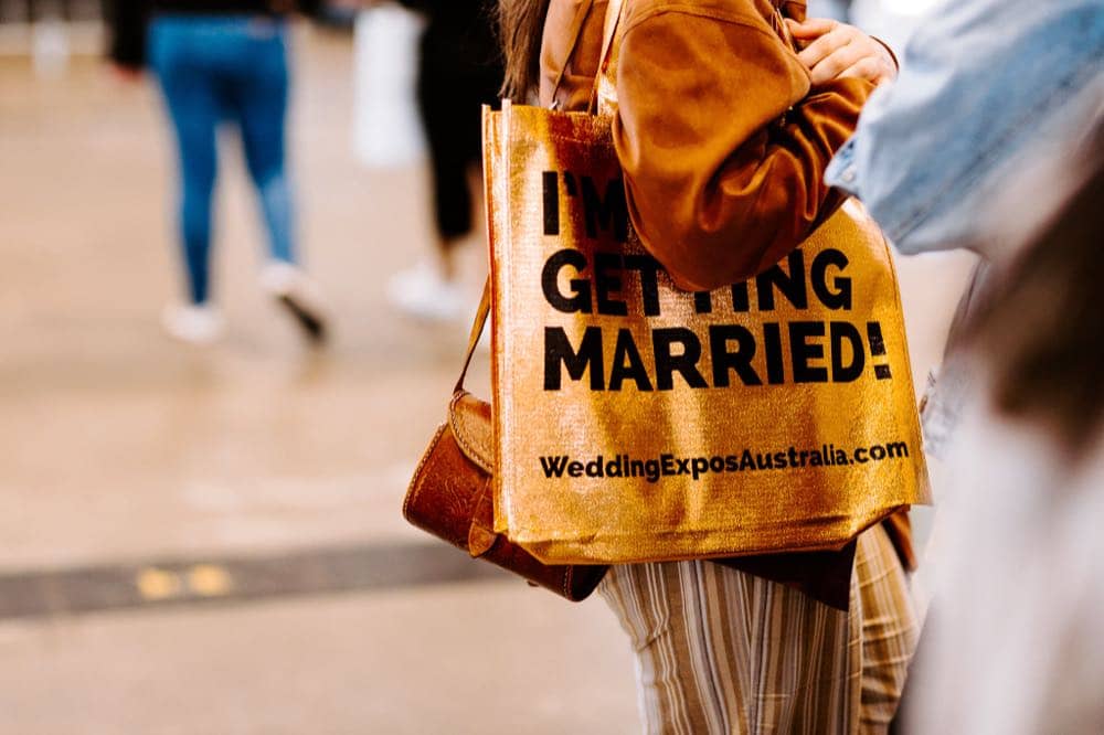 A couple carrying the gold “I'm Getting Married” bag at a Wedding Expos Australia event